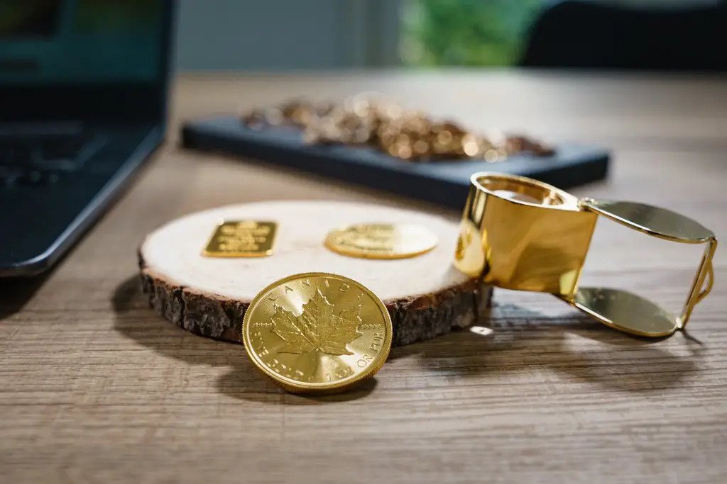 Vanhoja kultakoruja, kultaraha, kultaharkko ja suurennuslasi pöydällä